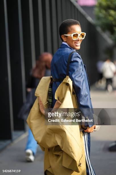 Tamu McPherson wears beige sunglasses, a navy blue embroidered logo pattern blazer jacket from Gucci x Adidas, matching navy blue embroidered logo...
