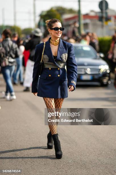 Guest wears black sunglasses, gold earrings, a gold large chain necklace from Versace, a gold large chain with oversized logo necklace from Gucci, a...