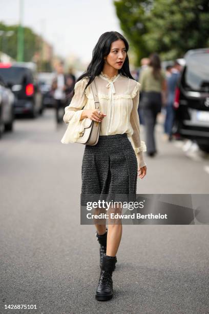 Guest wears a beige tulle ruffled details silk blouse, a beige matte leather shoulder bag, a dark gray tweed pleated short skirt, black shiny leather...