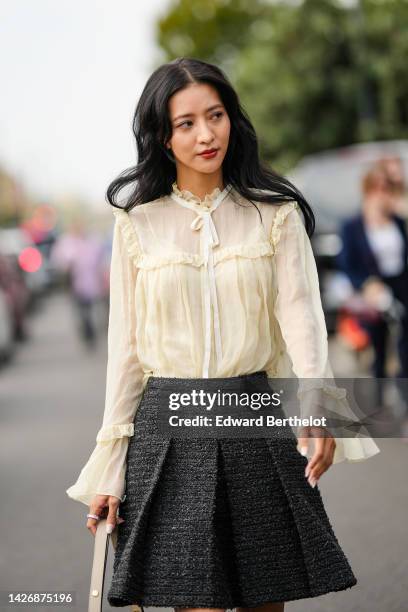 Guest wears a beige tulle ruffled details silk blouse, a beige matte leather shoulder bag, a dark gray tweed pleated short skirt, outside Gucci,...