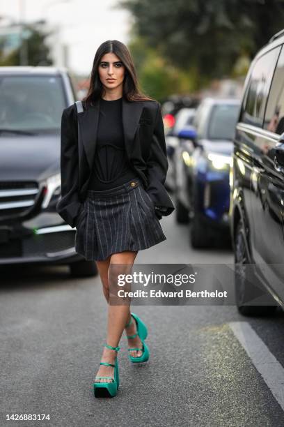 Guest wears black embossed corset pattern t-shirt, a black oversized blazer jacket, a black shiny leather shoulder bag, dark gray striped print...