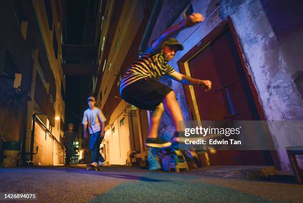 diversify young men skateboarding ollie back alley at night with friends - color enhanced stock pictures, royalty-free photos & images