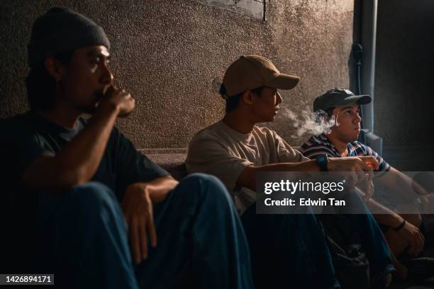 3 asian young man smoking sitting in a row at back alley at night with electronic cigarette - electronic cigarette 個照片及圖片檔