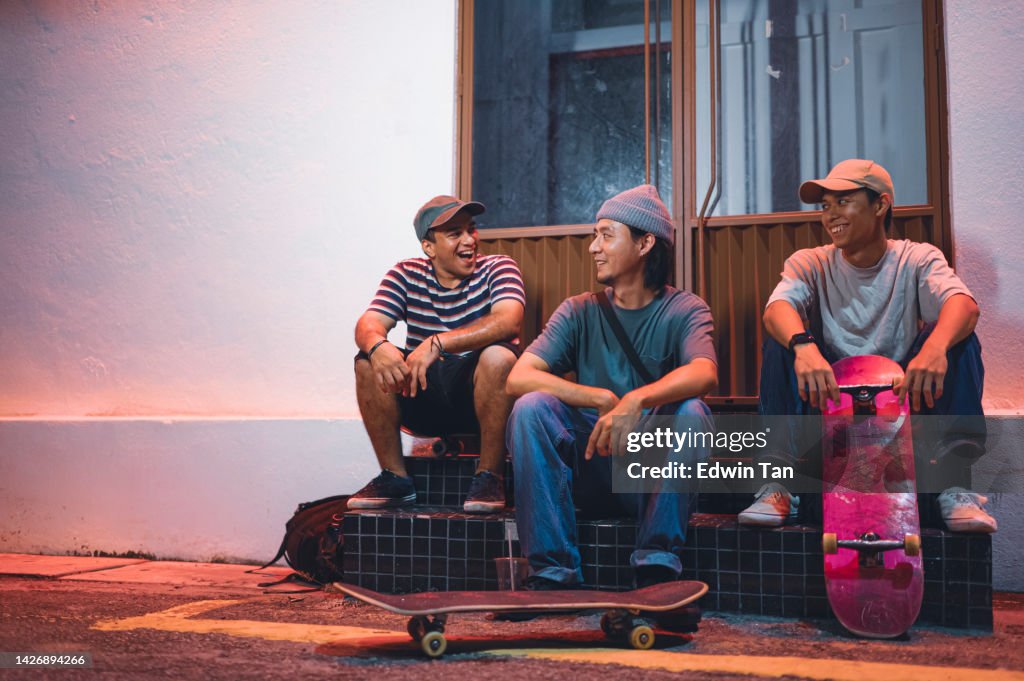 Asian young men sitting at back alley at night talking resting after skateboarding