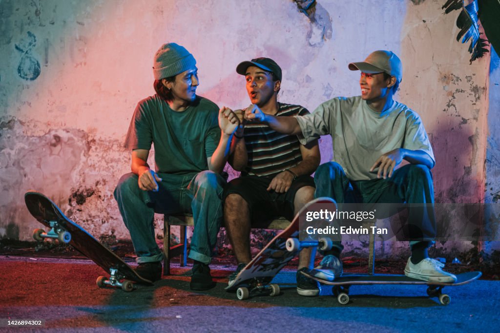 Diversify young men fist bump sitting at back alley at night with skateboard
