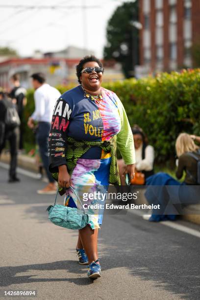 Guest wears black and white marble print pattern sunglasses from Balenciaga, a silver large cain with pendants necklace, a multicolored print pattern...