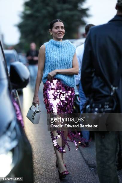 Guest wears gold earrings, a pale blue wool turtleneck / sleeveless pullover, a pink shiny mirror midi skirt, a white shiny leather Lady D-Light...