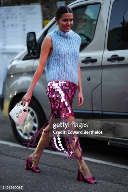 Guest wears gold earrings, a pale blue wool turtleneck / sleeveless pullover, a pink shiny mirror midi skirt, a white shiny leather Lady D-Light...