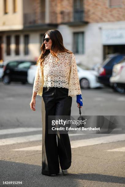 Guest wears black sunglasses from Ray Ban, a white lace print pattern flared long sleeves blouse, a royal blue mitten from Gucci x Adidas, a black...