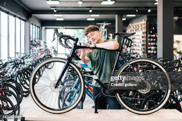 young man checking out at new bicycle in bikeshop - fietsenwinkel stockfoto's en -beelden