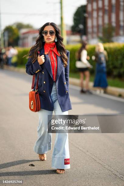Guest wears sunglasses, silver and crystal earrings, a red with white GG monogram print pattern silk scarf from Gucci, a red with black and white...