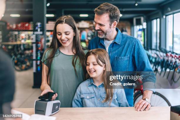 junge familie zahlt an der kasse mit handy - sportgeschäft stock-fotos und bilder