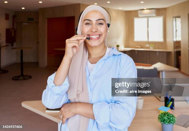 woman wearing a hiyab while working in the office, smiling and wearing headsets in her customer service work. - hiyab photos et images de collection