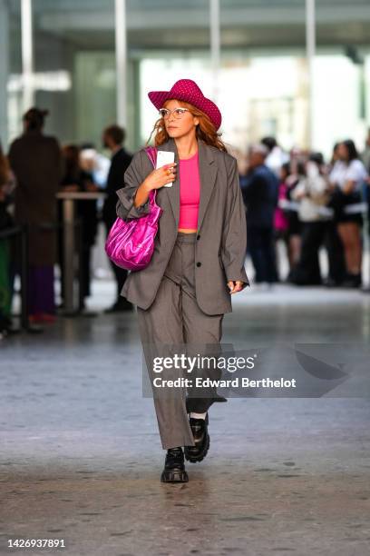 Guest wears a neon pink with embroidered rhienstones hat, glasses, pink and orange rings, a neon pink cropped top, a gray oversized blazer jacket,...