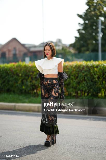 Tiffany Hsu wears a white large shoulder / cropped top, a black lace print pattern high gloves, a high waist black lace print pattern with...