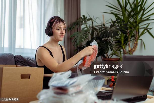 beautiful woman opening a cardboard box in the living room and holding a product - marketing material stock pictures, royalty-free photos & images