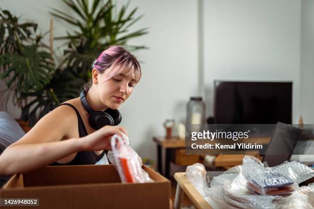 beautiful woman opening a cardboard box in the living room and holding a product - marketing material stock pictures, royalty-free photos & images