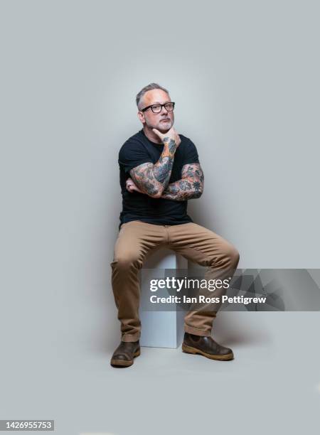 middle-aged tattooed man deep in thought - man portrait full body 50's stock-fotos und bilder