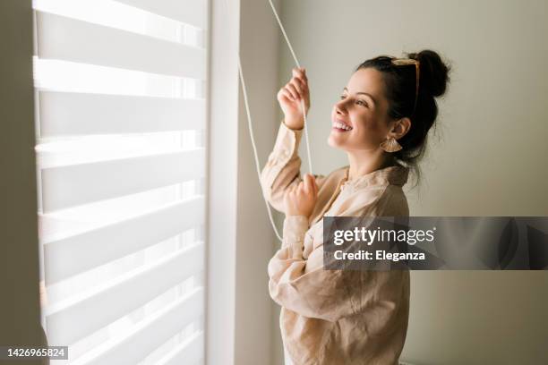 beautiful young woman looking through the window - window curtains stock pictures, royalty-free photos & images