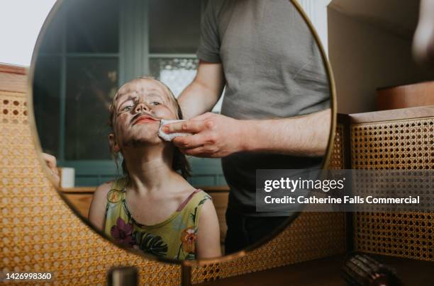 a mischievous little girl has doodled all over her face with make-up and her father is wiping it off - dirty mirror stock pictures, royalty-free photos & images