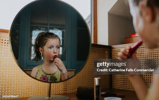 a mischievous young girl uses her mothers lipstick - schoolmeisje stockfoto's en -beelden