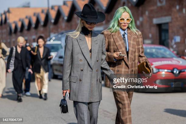 Vanessa Hong wears grey double breasted suit, black hat & Tina Leung wears checkered brown suit, tie outside Gucci during the Milan Fashion Week -...