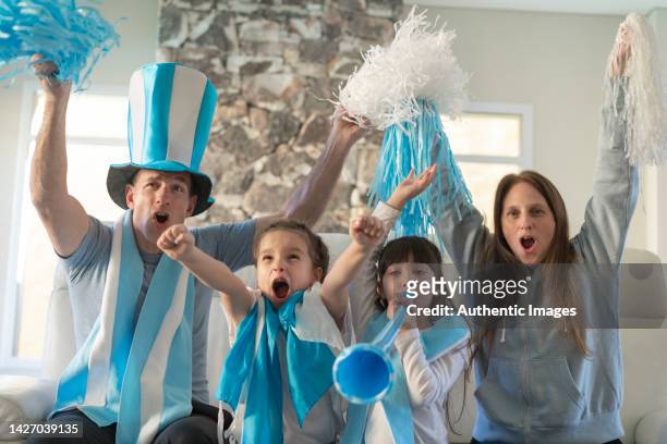 retrato de la familia argentina fanática del fútbol viendo felizmente el partido de fútbol en la televisión en casa y celebrando un gol - argentina fan fotografías e imágenes de stock