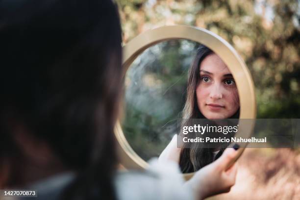 beautiful young girl in a white dress looking her reflection in a round mirror. self-love concept - vanity lights stock pictures, royalty-free photos & images