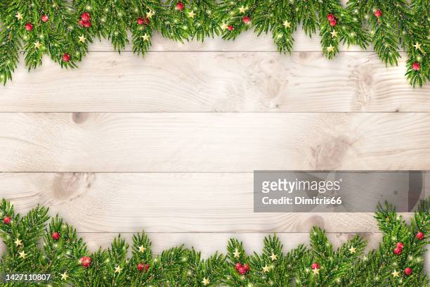 christmas and new year background with fir branches, glitter, christmas ornaments and lights on rustic wooden planks - holiday stock illustrations