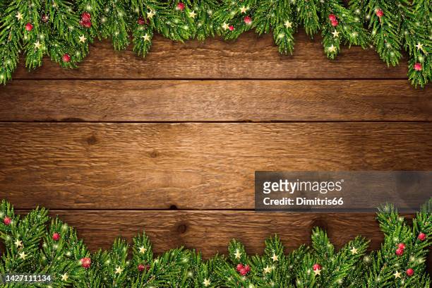 christmas and new year background with fir branches, glitter, christmas ornaments and lights on rustic wooden planks - holiday stock illustrations
