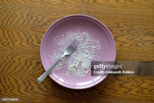 a dirty empty plate and fork on a wooden kitchen or dining table. cutlery is used, symbolizing the end of lunch or dinner. a portion of food eaten, overeating. - messy table after party stock-fotos und bilder