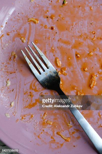 a dirty empty plate and fork on a wooden kitchen or dining table. cutlery is used, symbolizing the end of lunch or dinner. a portion of food eaten, overeating. - cleaning after party - fotografias e filmes do acervo