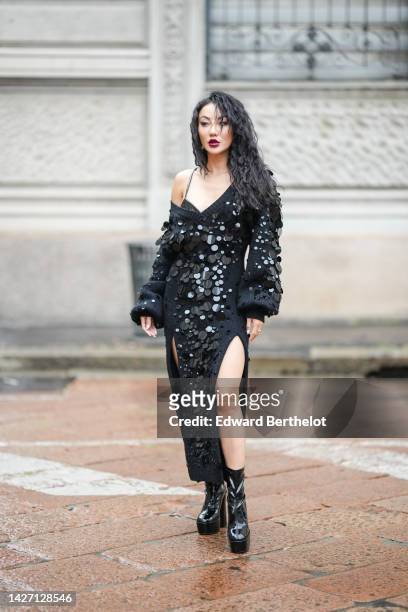 Jessica Wang wears earrings, a black shiny varnished leather bra underwear, a black wool with embroidered large sequined / asymmetric shoulder-off /...