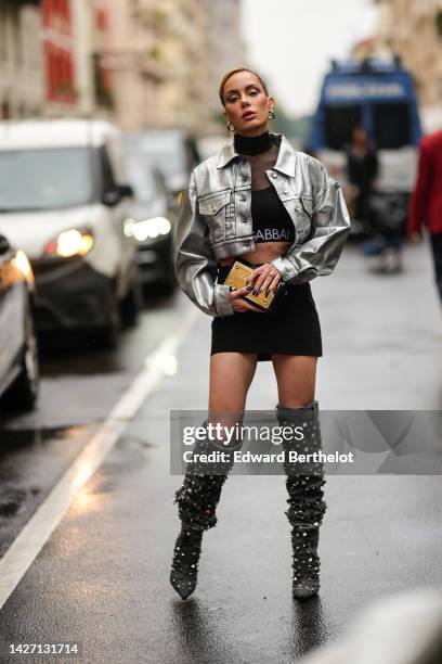 Sira Pevida wears silver large earrings, a black turtleneck with tulle neck / cropped top from Dolce & Gabbana, a silver shiny leather cropped blazer...