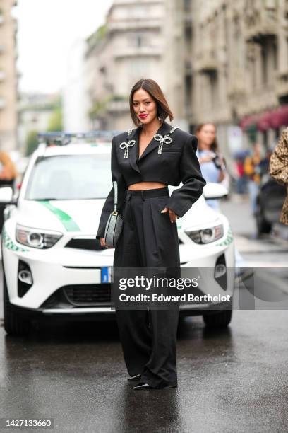 Tiffany Hsu wears a black backless / cropped blazer jacket with embroidered large crystal jewels knot and logo from Area, black large wide legs suit...