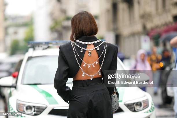 Tiffany Hsu wears a black backless / cropped blazer jacket with embroidered large crystal jewels knot and logo from Area, black large wide legs suit...