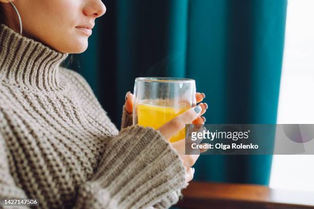 energy crisis. woman dressed in a warm sweater drinking hot orange tea - flu season stock pictures, royalty-free photos & images