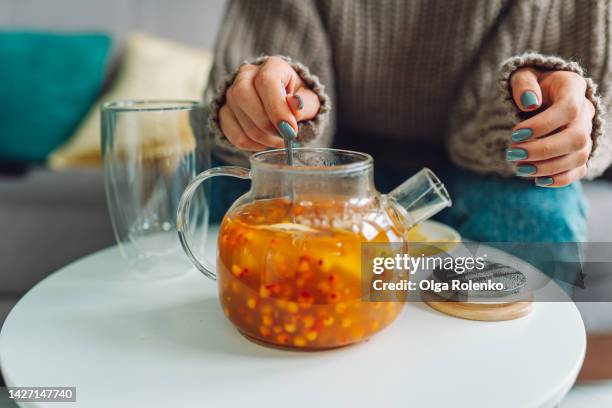 vitaminization, maintenance of immunity. frozen woman in warm sweater stirs hot orange berry tea at home - buckthorn stock pictures, royalty-free photos & images