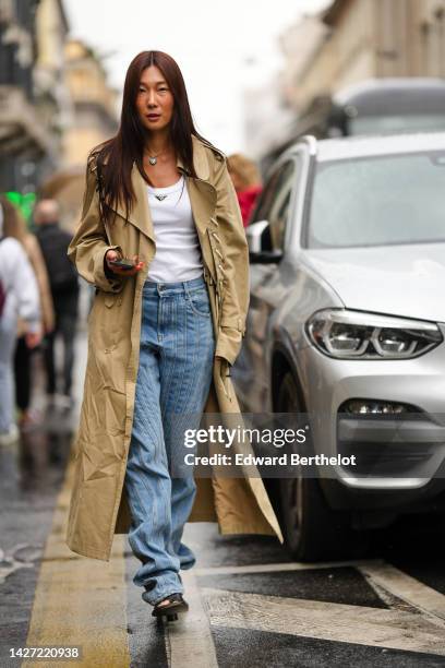 Guest wears a gold chain with black pearl heart pendant necklace from Chanel, a white tank-top from Prada, a beige long laces details trench coat,...