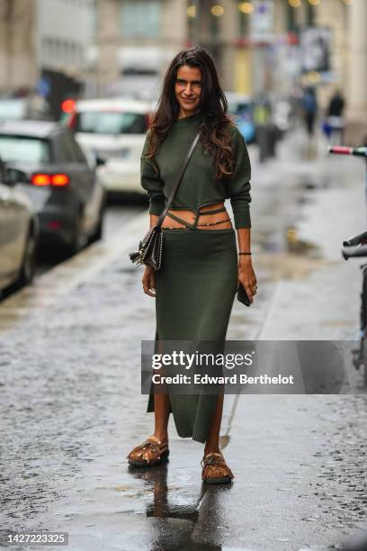 Guest wears a khaki long sleeves laces waist wool pullover, a matching khaki lace waist long wool skirt, a black shiny leather crossbody bag, rings,...