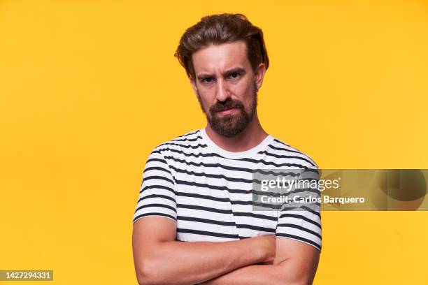 close up photo of an angry caucasian man, standing  crossing arms and looking at camera. isolated in yellow background. - young face serious at camera stockfoto's en -beelden