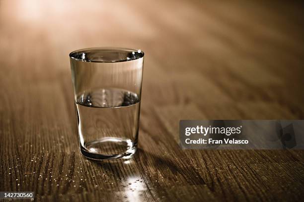 half-filled glass of water on table - half stockfoto's en -beelden