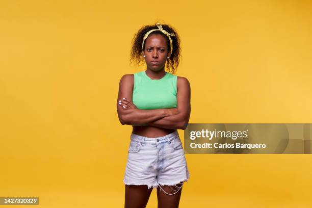 photo of an angry latin woman standing against a yellow background crossing arms and looking at camera seriously. isolated image at studio. - neid stock-fotos und bilder