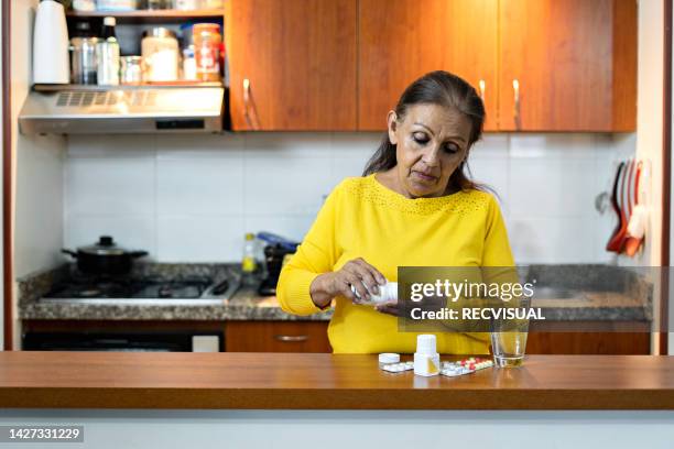 mujer mayor con una pastilla en la mano en la cocina. - usar la boca fotografías e imágenes de stock