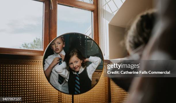 siblings prepare for school, looking in the mirror as they fix their ties - school tie stockfoto's en -beelden