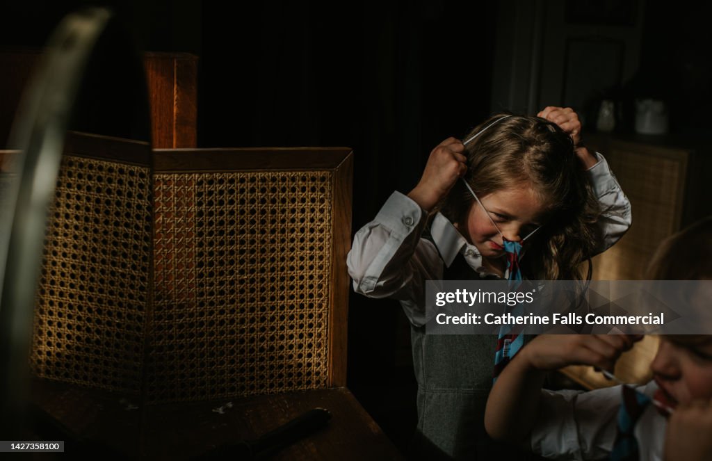 A little girl pulls an elasticated school tie over her head as she gets ready for school in the morning