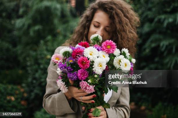 young woman with long curly hair holding colorful autumn aster flower bunch on the street - autumn bouquet stock pictures, royalty-free photos & images