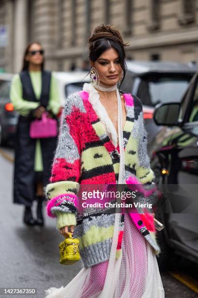 Angela Rozas Saiz wears oversized colorful striped cardigan with pattern in beige, grey, pink, red, white see trough dress, pink heels, golden bag...