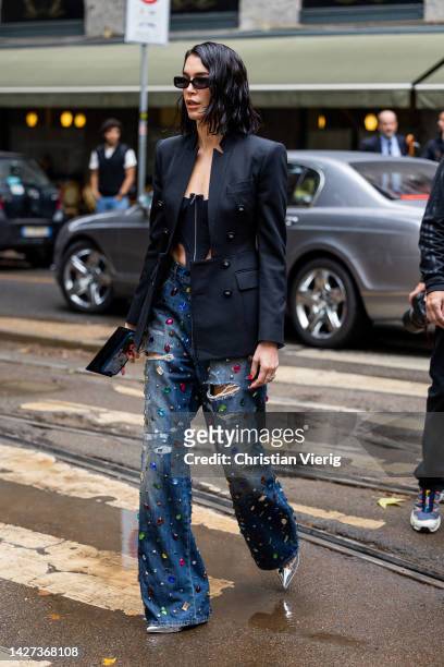 Brittany Xavier wears black cut out top, studded ripped blue washed denim jeans, black tailored double breasted blazer outside Dolce & Gabbana during...