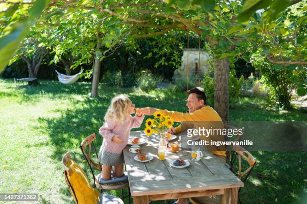 father feeding daughter with melon while having breakfast in the garden - french garden imagens e fotografias de stock